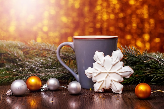 Weihnachts- und Neujahrskarte mit Keksen neben einer Tasse heißen Tees und einem Tannenzweig mit Weihnachtsschmuck und glänzendem Bokeh-Hintergrund