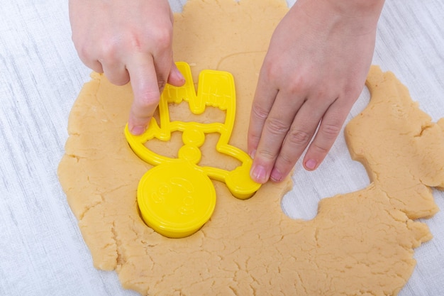 Weihnachts- und Silvestertradition. Familienhaus Bäckerei. Kochen traditioneller Lebkuchenplätzchen. Kinderhände schneiden rohe Lebkuchenteigplätzchen in Form eines Weihnachtsmannes auf dem Tisch zu Hause