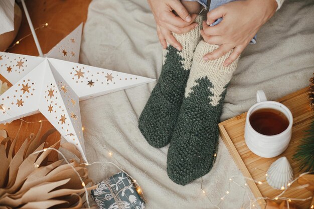 Foto weihnachts-winter-hygge frauenbeine in warmen socken auf decke tee weihnachtssterne leuchten bäume