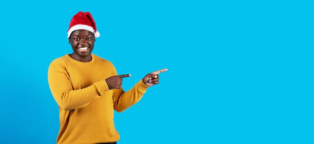 Weihnachtsangebot Fröhlicher schwarzer Kerl in Weihnachtsmütze, der auf Textfreiraum zeigt
