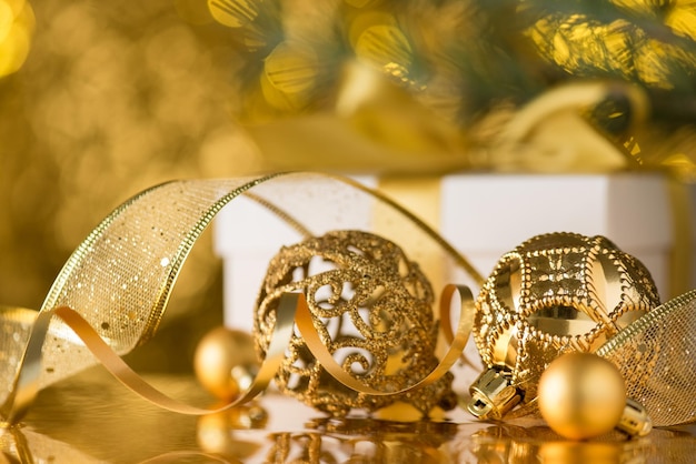 Foto weihnachtsatmosphäre kreatives konzept nahaufnahme foto von goldenen christbaumschmuck ornamenten kugeln serpentinenband weiße geschenkbox und kiefernzweig auf glänzend goldenem bokeh hintergrund