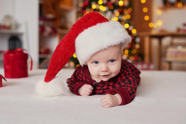 Weihnachtsbaby in Sankt-Hut auf dem Hintergrund des Weihnachtsbaums mit Geschenken.