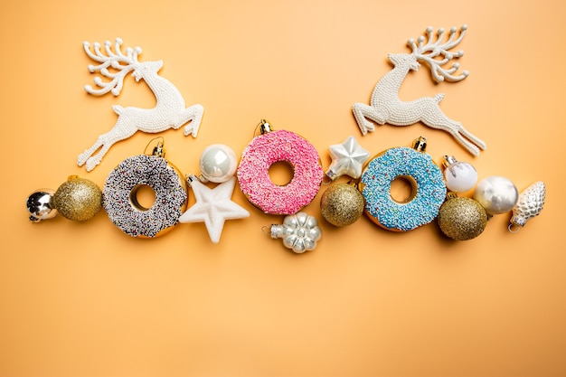 Weihnachtsbanner mit spielzeugglasiertem Donut und Weihnachtsdekorationen Draufsicht orange pastellfarbenem Hintergrund