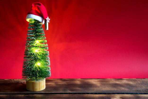 Weihnachtsbaum auf rotem Grund mit Lichtern aus Girlanden, karamellgestreiften Zuckerrohr, Weihnachtsmütze, Lametta. Neujahr, festliche Atmosphäre. Platz kopieren