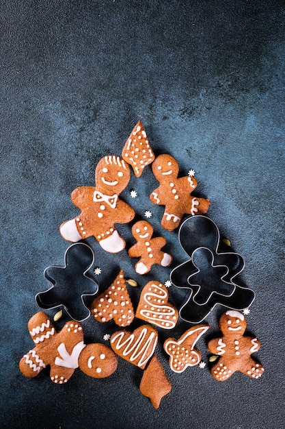 Weihnachtsbaum aus Lebkuchen auf dunkelblauem Hintergrund mit Kopienraum für Text. Lebkuchenplätzchen mit Küchenutensilien. Neujahrs- und Weihnachtspostkarte. Verschiedene Kekse.