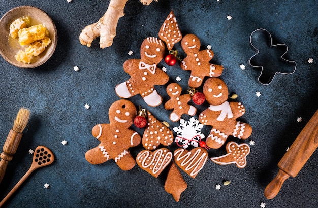 Weihnachtsbaum aus Lebkuchen auf dunkelblauem Hintergrund mit Kopienraum für Text. Lebkuchenplätzchen mit Küchenutensilien. Neujahrs- und Weihnachtspostkarte. Verschiedene Kekse.