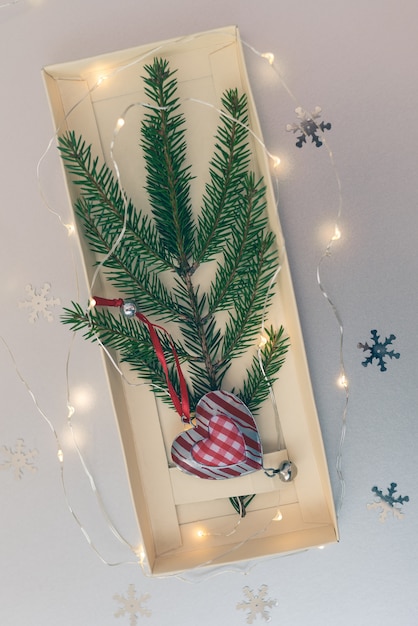 Weihnachtsbaum decoratin rotes Herz und helle Girlande des natürlichen Tannenzweigs der Fichte auf Weißbuch