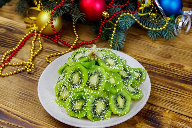 Weihnachtsbaum geformter Obstsalat und Weihnachtsschmuck auf Holztisch. Kreative Idee für festliche Desserts zu Weihnachten und Neujahr. Lustige Essensidee für Kinder