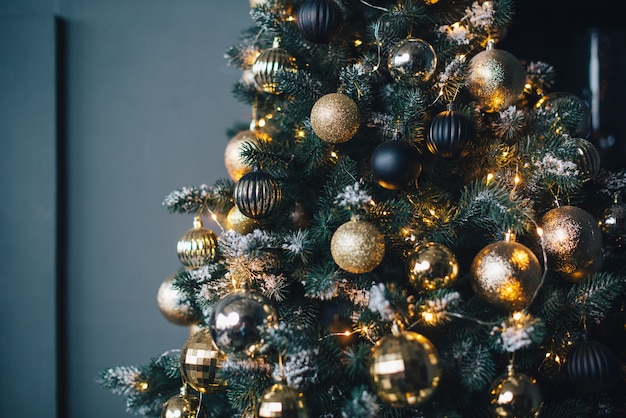 Weihnachtsbaum geschmückt mit Girlanden und goldenen Kugeln an einer dunklen Wand