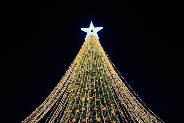 Weihnachtsbaum mit dekorativen Birnen der gelben Girlanden und großem weißem Sterndeckel am blauen Nachthimmel