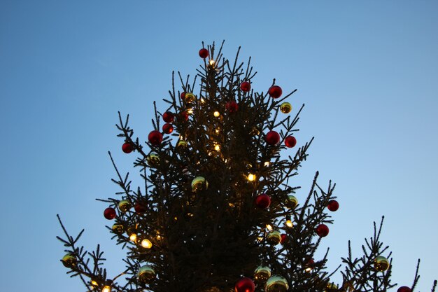 Weihnachtsbaum mit roten Luftballons und Lichterketten vor blauem Himmel