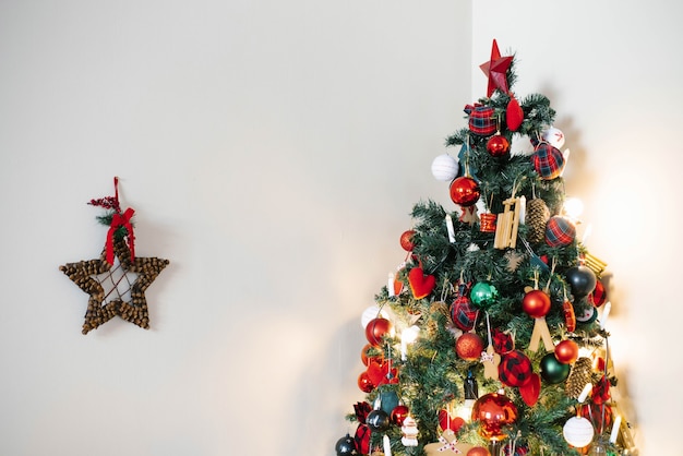 Weihnachtsbaum mit roten Spielzeugen und grünen auf einem hellen Wandhintergrund