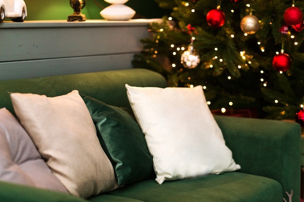 Weihnachtsbaum mit roten und gelben Kugeln und grünem Sofa mit Kissen