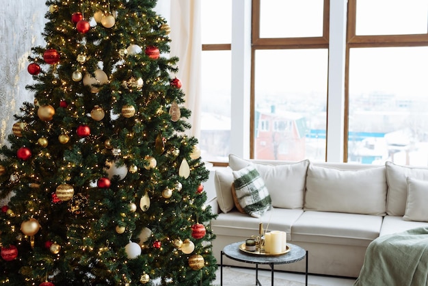 Weihnachtsbaum mit roten und goldenen Kugeln und goldenen Lichterketten in einem hellen Raum