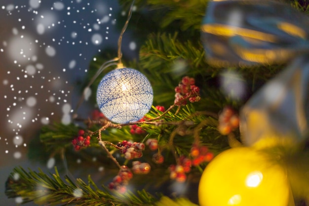 Weihnachtsbaum mit Spielzeug geschmückt. Weihnachtsdekoration in der Natur, Bogen, Bälle, rote Beeren. Abend schneereichen Winter. Brennende bunte Girlande