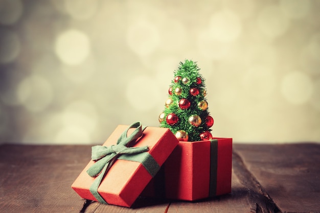 Weihnachtsbaum und rote Geschenkbox auf Holztisch mit Bokeh im Hintergrund