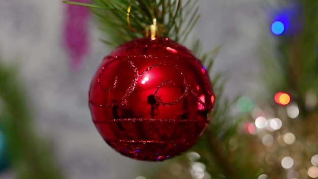 Weihnachtsbaum verziert mit roter Glaskugel auf Weihnachtsfichtenzweig auf Hintergrundbokeh von flackernden Glühbirnengirlanden