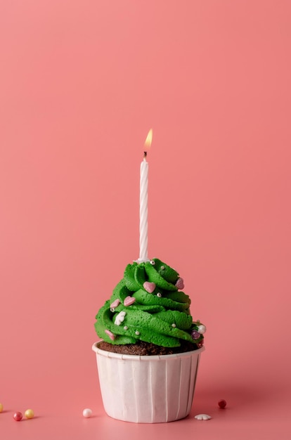 Weihnachtsbaumförmiger Cupcake mit einer Kerze auf rosa Hintergrund