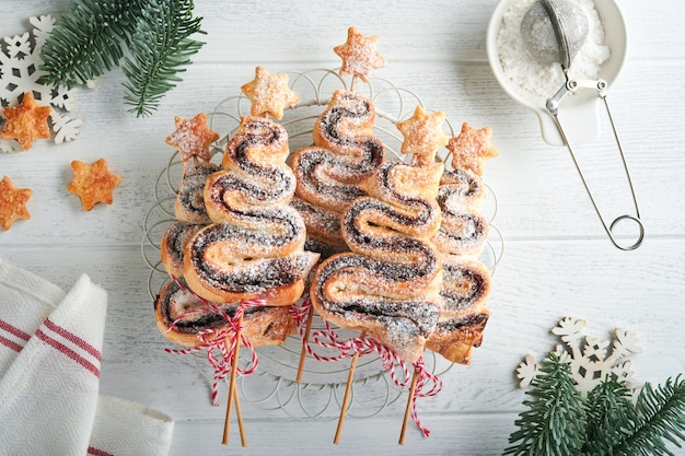 Weihnachtsbaumform Blätterteigkuchen mit Schokoladenfüllung Zuckerpulver und Lutscher auf altem weißem Holzhintergrund Weihnachten Neujahr Appetizer Festliche Idee für Weihnachten oder Neujahr Abendessen