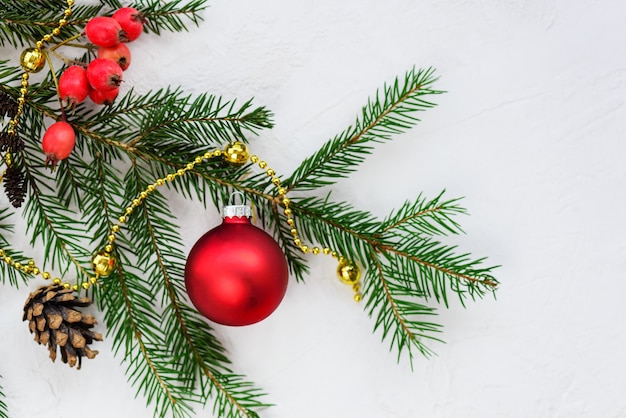 Weihnachtsbaumzweig mit einer roten Kugel auf einem hellen Hintergrund.
