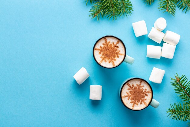 Weihnachtscappuccino mit Schneeflocke gemacht mit Zimt nahe Marshmallows auf blauem Hintergrund