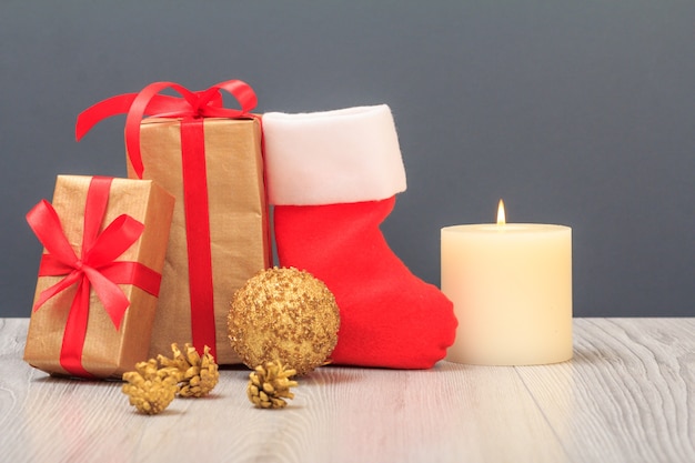 Weihnachtsdekoration. Geschenkboxen, Santa's Boot, Spielzeugball, Kegel und brennende Kerze auf grauem Hintergrund. Weihnachtsgrußkartenkonzept.
