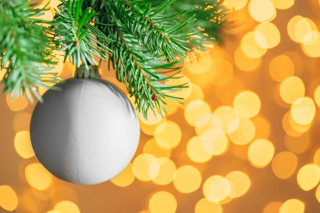 Weihnachtsdekoration hängt an einem Tannenzweig gegen Weihnachtsbeleuchtung