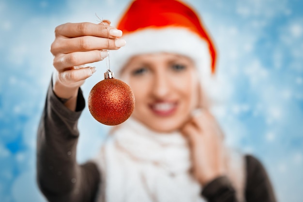 Weihnachtsdekoration in der Hand einer schönen jungen lächelnden Frau. Selektiver Fokus. Konzentrieren Sie sich auf den Vordergrund, auf Weihnachtskugel.