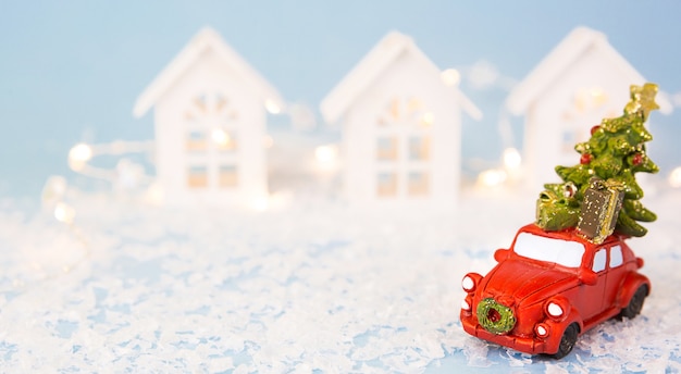 Weihnachtsdekoration - rotes Retro-Auto auf Schnee trägt Weihnachtsbaum in der Nähe von Häusern