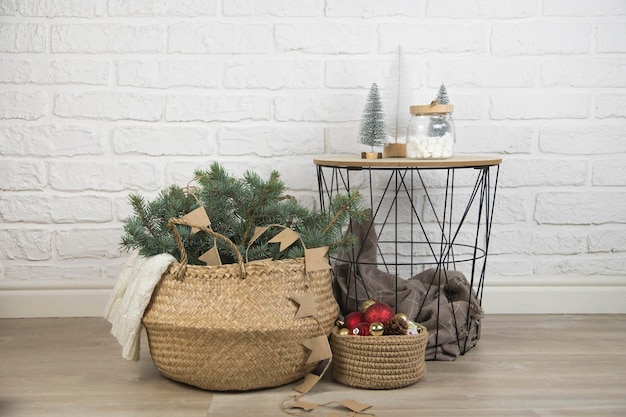 Weihnachtsdekoration rustikaler Strohkorb mit Tannenzweigen gestrickter Korb mit Weihnachtsspielzeug und Couchtisch auf Backsteinhintergrund