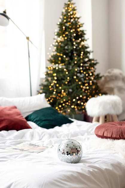 Weihnachtsdekoration. Schlafzimmer in hellen Farben mit großem Bett. Das Interieur ist mit Girlanden, Weihnachtskränzen und einem Neujahrsbaum im modernen Stil geschmückt. Weicher selektiver Fokus.