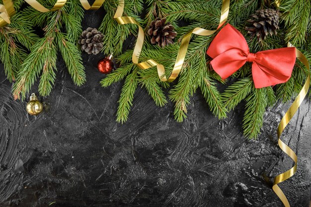 Weihnachtsdekoration. Tannenzweig mit Kugeln, Geschenken, Tannenzapfen und Bögen auf einer schwarzen Holzoberfläche