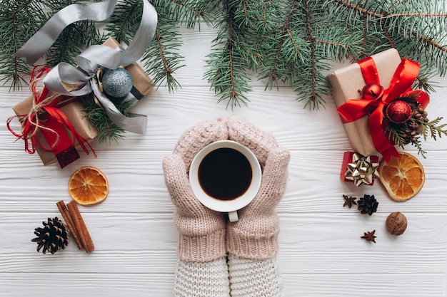 Weihnachtsdekorationen, -geschenke und -lebensmittel auf einem weißen hölzernen Hintergrund. Trinkender Kaffee der Frau.