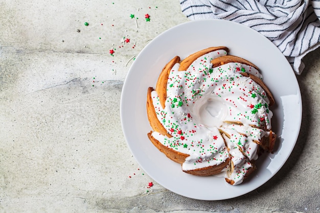 Weihnachtsdessert Vanille-Pfund-Kuchen mit Zuckerguss und festlichen farbigen Streuseln auf weißem Plattengrauhintergrund