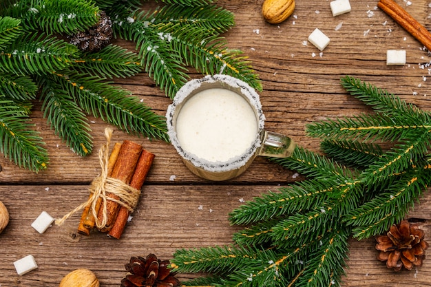 Weihnachtseierlikör oder Cola de Mono Cocktail. Klassisches Wintergetränk im Glasbecher, Weihnachtsdekorationen. Immergrüne Zweige, Zimt, Walnüsse, Zucker.