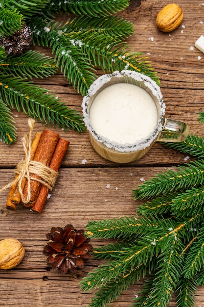 Weihnachtseierlikör oder Cola de Mono Cocktail. Klassisches Wintergetränk im Glasbecher, Weihnachtsdekorationen. Immergrüne Zweige, Zimt, Walnüsse, Zucker.