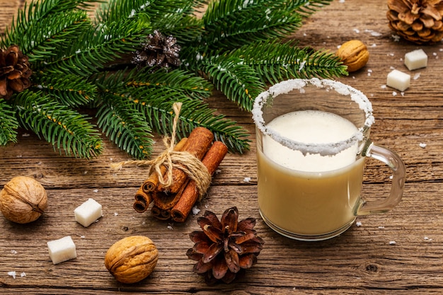Weihnachtseierlikör oder Cola de Mono Cocktail. Klassisches Wintergetränk im Glasbecher, Weihnachtsdekorationen. Immergrüne Zweige, Zimt, Walnüsse, Zucker.