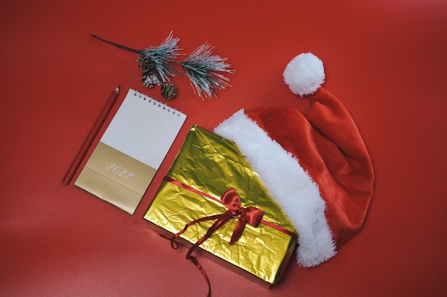 Weihnachtseinkauf. Liste der Einkäufe und Geschenke für das neue Jahr. Der Weihnachtsmann-Hut liegt auf einem goldenen Kasten auf rotem Grund.