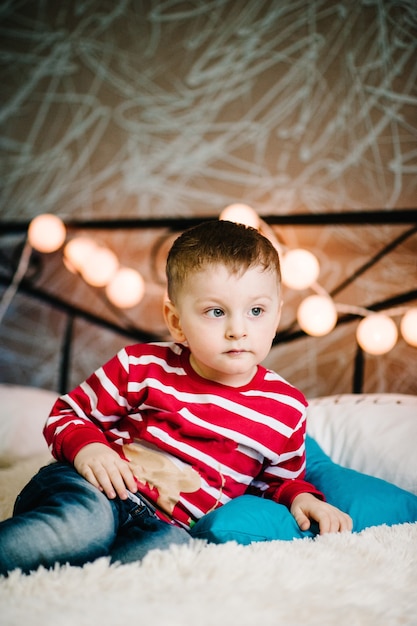 Weihnachtsfamilie! Glücklicher kleiner Sohn in Weihnachtsmannpullovern, spielen mit Kissen.