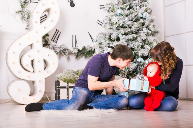 Weihnachtsfamilie mit Babyöffnungsgeschenken. Glücklich lächelnde Eltern und Kind zu Hause feiern Neujahr