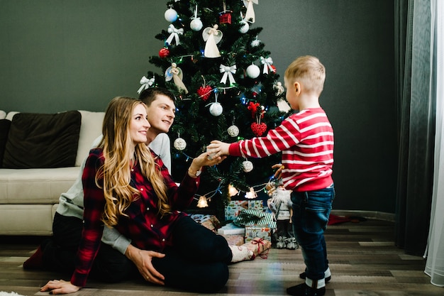 Weihnachtsfamilie offen Geschenk Geschenkbox, Nacht Weihnachten. Frohe Weihnachten und schöne Feiertage! Familie, die Geschenke austauscht. Eltern und kleine Kinder in der Nähe von Weihnachtsbaum drinnen.