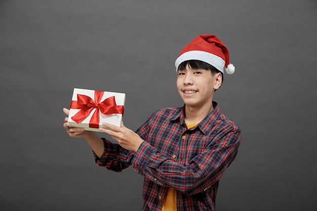 Weihnachtsfeier und Feiertagskonzept. junger asiatischer Mann mit Geschenkbox Studioaufnahme, auf grauem Hintergrund isoliert