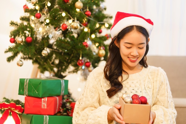 Weihnachtsfeierkonzept Asiatische Frau in Weihnachtsmütze hält eine Schachtel Weihnachtskugel zur Dekoration