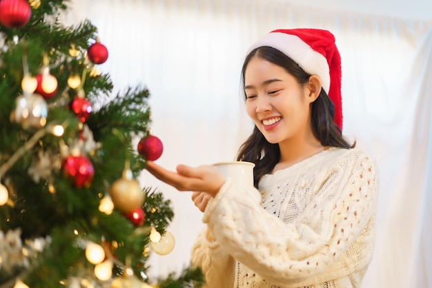 Weihnachtsfeierkonzept Asiatische Frau trinkt Kaffee und sieht Weihnachtsbaum mit Glück aus