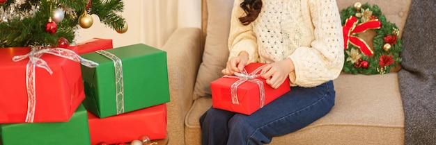 Weihnachtsfeierkonzept Junge asiatische Frau, die auf der Couch sitzt und Weihnachtsgeschenk öffnet