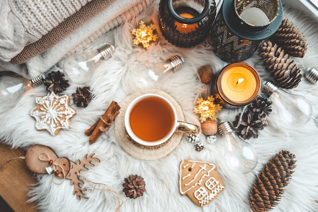 Weihnachtsfeiertagsdekor flach Draufsicht Tasse Tee brennende Kerzen Lebkuchenkegel und Zimt auf einem flauschigen Plaid
