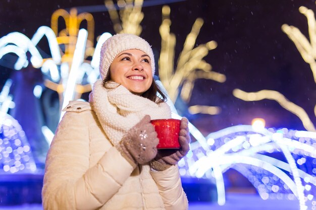 Weihnachtsferien schöne lächelnde Frau in warmer Kleidung mit Tasse heißem Kaffee im Freien im Winter