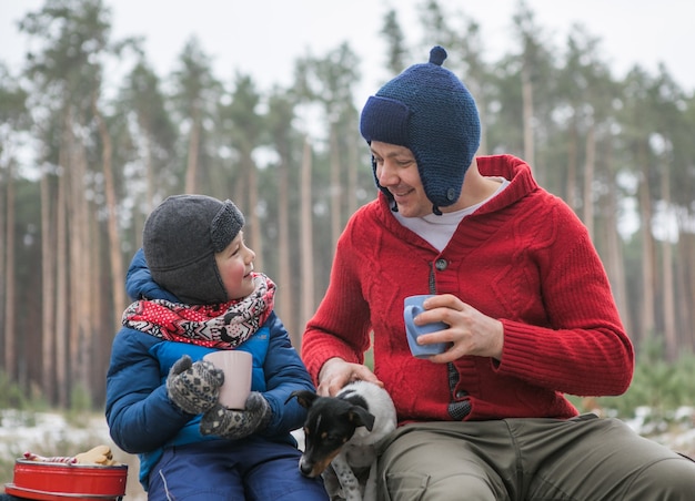 Weihnachtsferien, Vater und Sohn trinken heißes Neujahrsgetränk. Glückliche Familie bei einem Spaziergang im Freien im sonnigen Winterwald