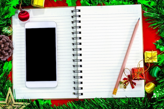 Weihnachtsfestliche Dekorationen mit leerem Smartphone, Notizbuch und Bleistift auf rotem Papier-backg