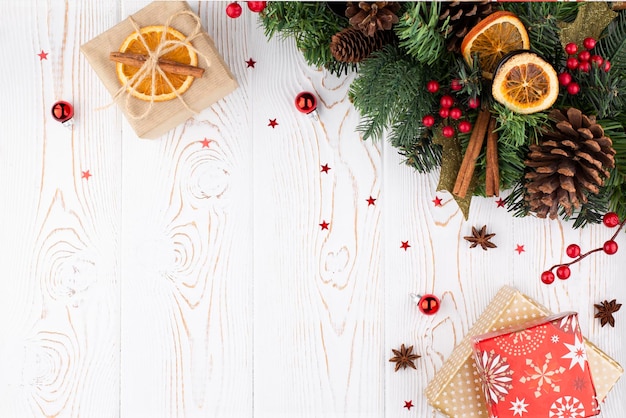 Weihnachtsfestlicher Hintergrund mit Tannenbaum, verziert mit Tannenzapfenperlen und Geschenken, eingewickelt in Kraftpapier, getrocknete Orangen auf weiß getünchtem weißem Holzhintergrund im rustikalen Stil, flacher Kopienraum